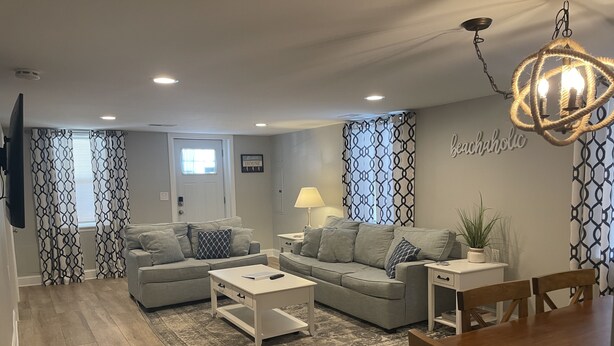 A modern living room with two grey sofas, a white coffee table, a wooden dining table, and a chandelier. - Sea Level Sanctuary's Low Tide in Seaside Park (Seaside Park)