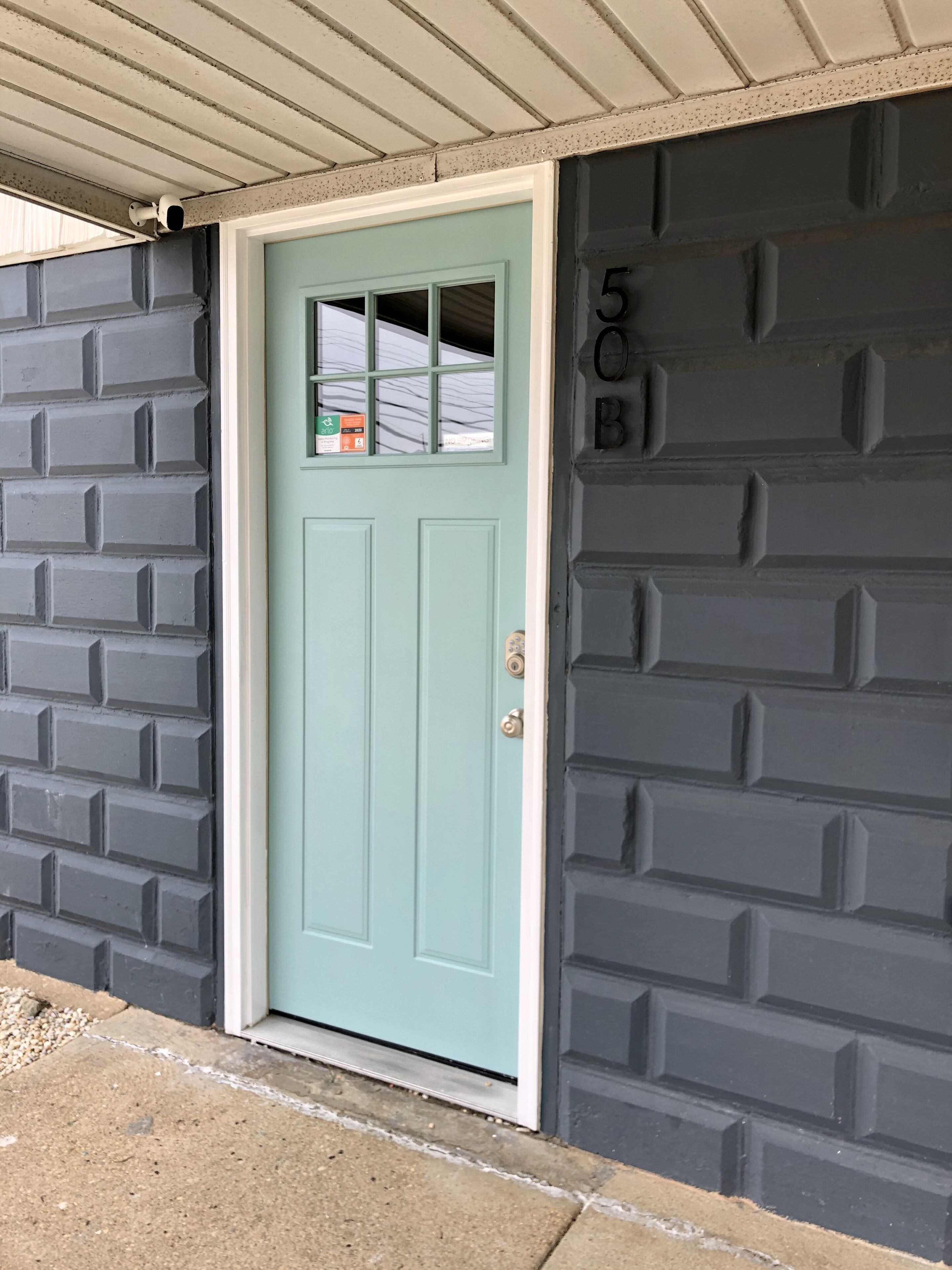 A light blue door with a small window, a mailbox, and a mailbox with a green and orange sticker.