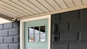 A light blue door with a small window, a mailbox, and a mailbox with a green and orange sticker. - Sea Level Sanctuary's Low Tide in Seaside Park (Seaside Park)