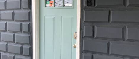 A light blue door with a small window, a mailbox, and a mailbox with a green and orange sticker.