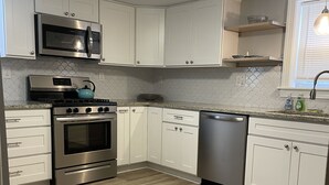 A modern kitchen with white cabinets, stainless steel appliances, and a herringbone-patterned backsplash. - Sea Level Sanctuary's Low Tide in Seaside Park (Seaside Park)