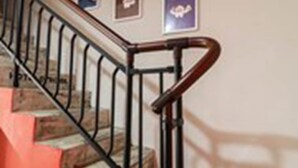 Una escalera con barandilla de madera y balaustres metálicos, que conduce a un rellano con tres certificados o premios enmarcados en la pared.