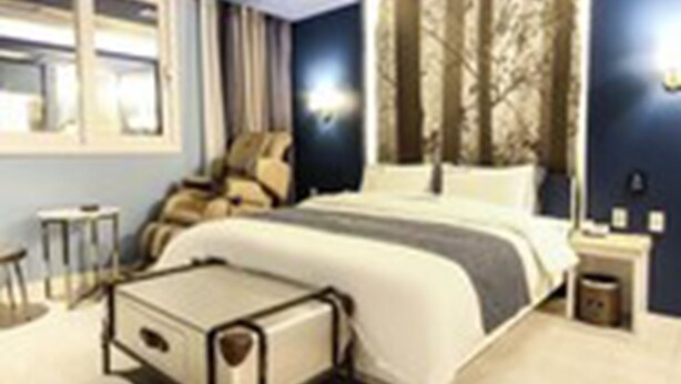 Habitación de hotel moderna con cama, mesitas de noche, una silla y vistas al exterior.