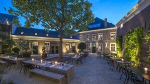 An outdoor dining area with tables and chairs, surrounded by brick buildings and trees. - Hotel Kazerne (Eindhoven)
