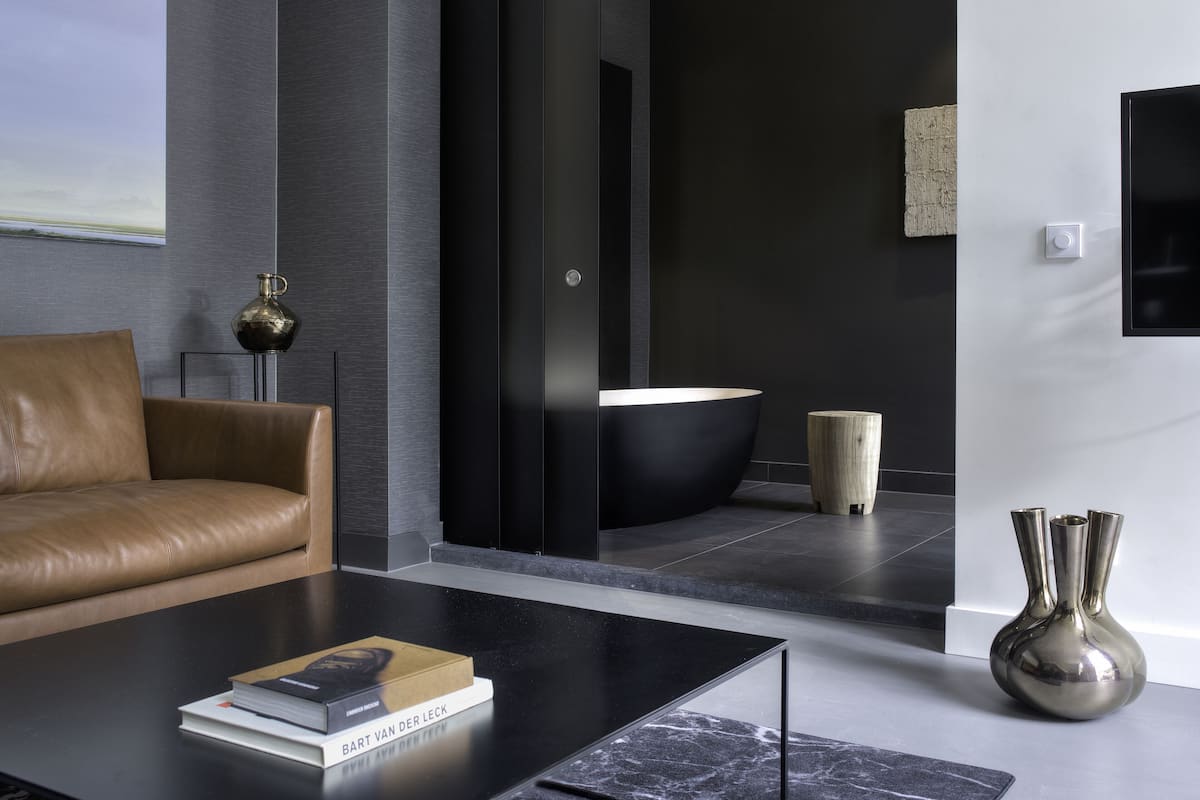 A modern living room with a leather sofa, a black coffee table with a book, a black bathtub, and a wooden stool.