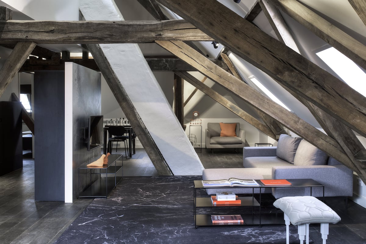 An attic room with exposed wooden beams, a sofa, a coffee table, and a fireplace.
