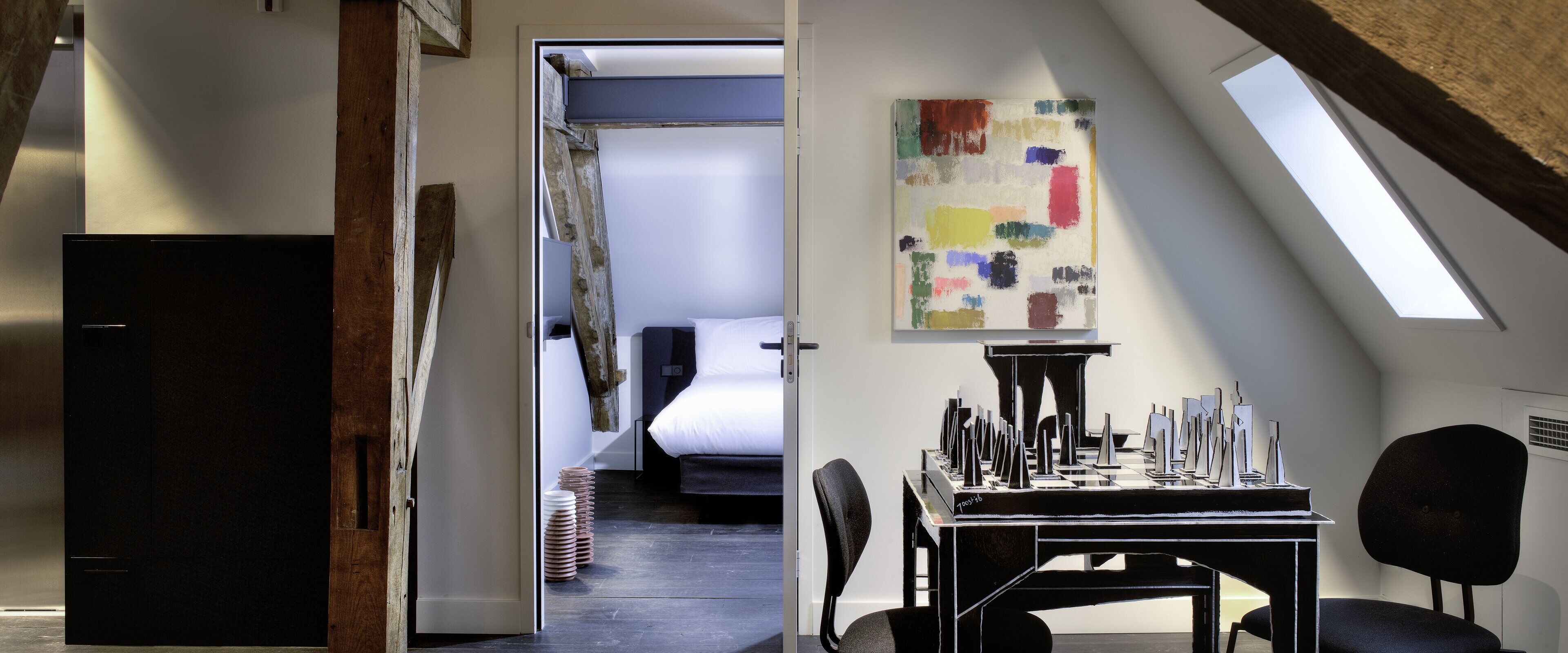 Una habitación moderna con cama, un escritorio y piezas de ajedrez, y un tragaluz.