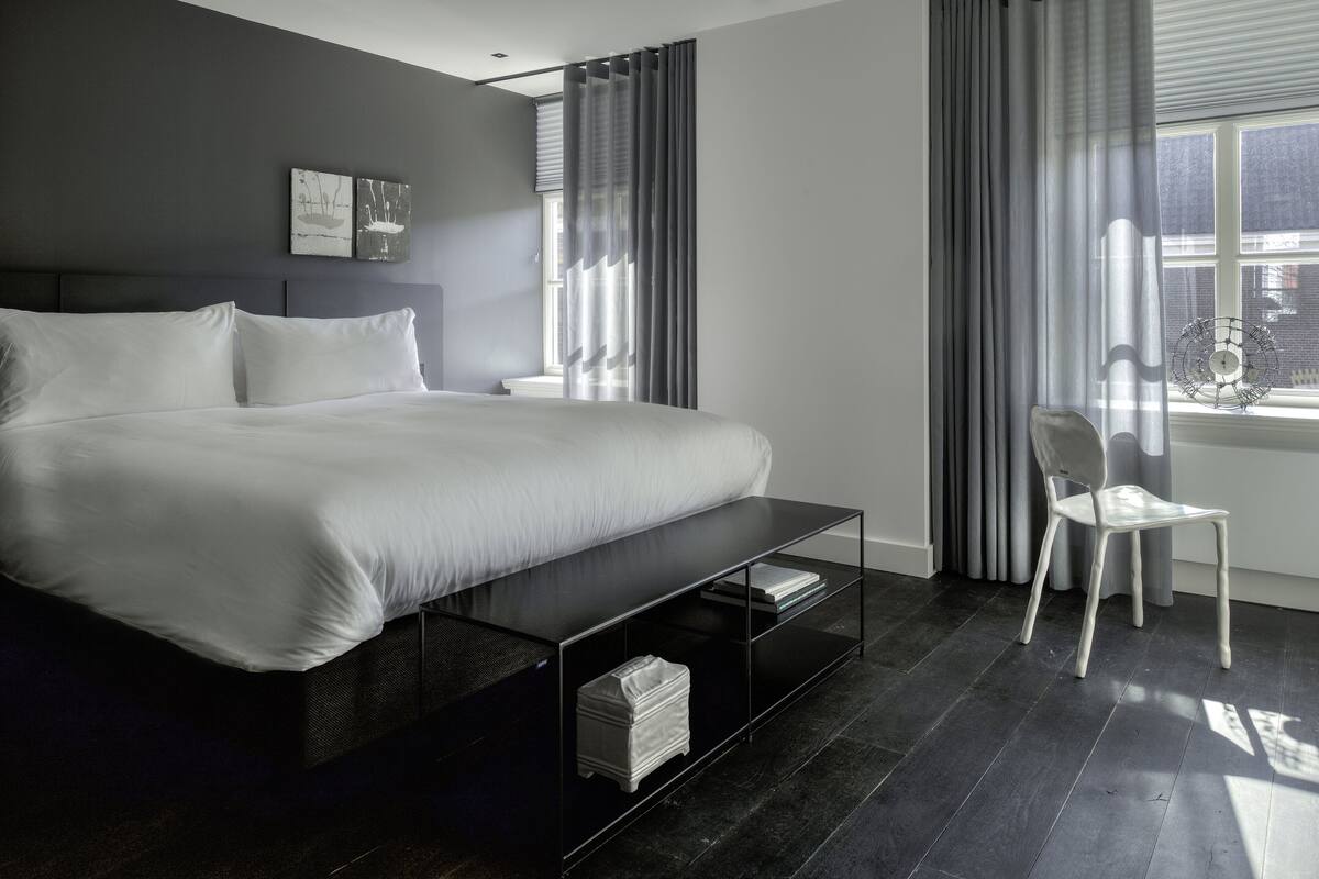 A modern bedroom with a large bed, a bedside table, a chair, and a window with curtains.