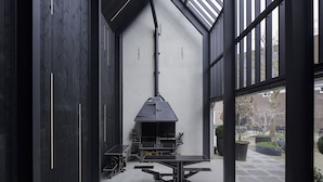 A modern outdoor dining area with a black grill, tables, and chairs, surrounded by large windows and a brick wall. - Hotel Kazerne (Eindhoven)