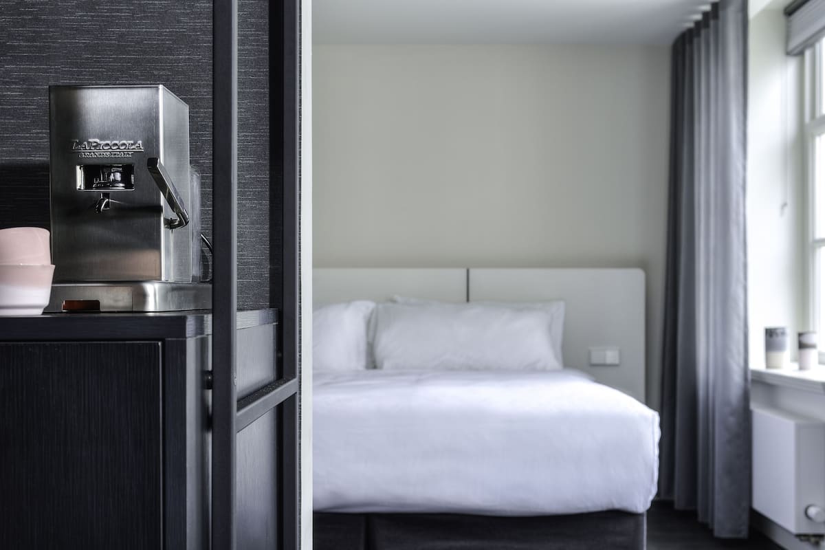A hotel room with a bed, a coffee machine, and a window with curtains.