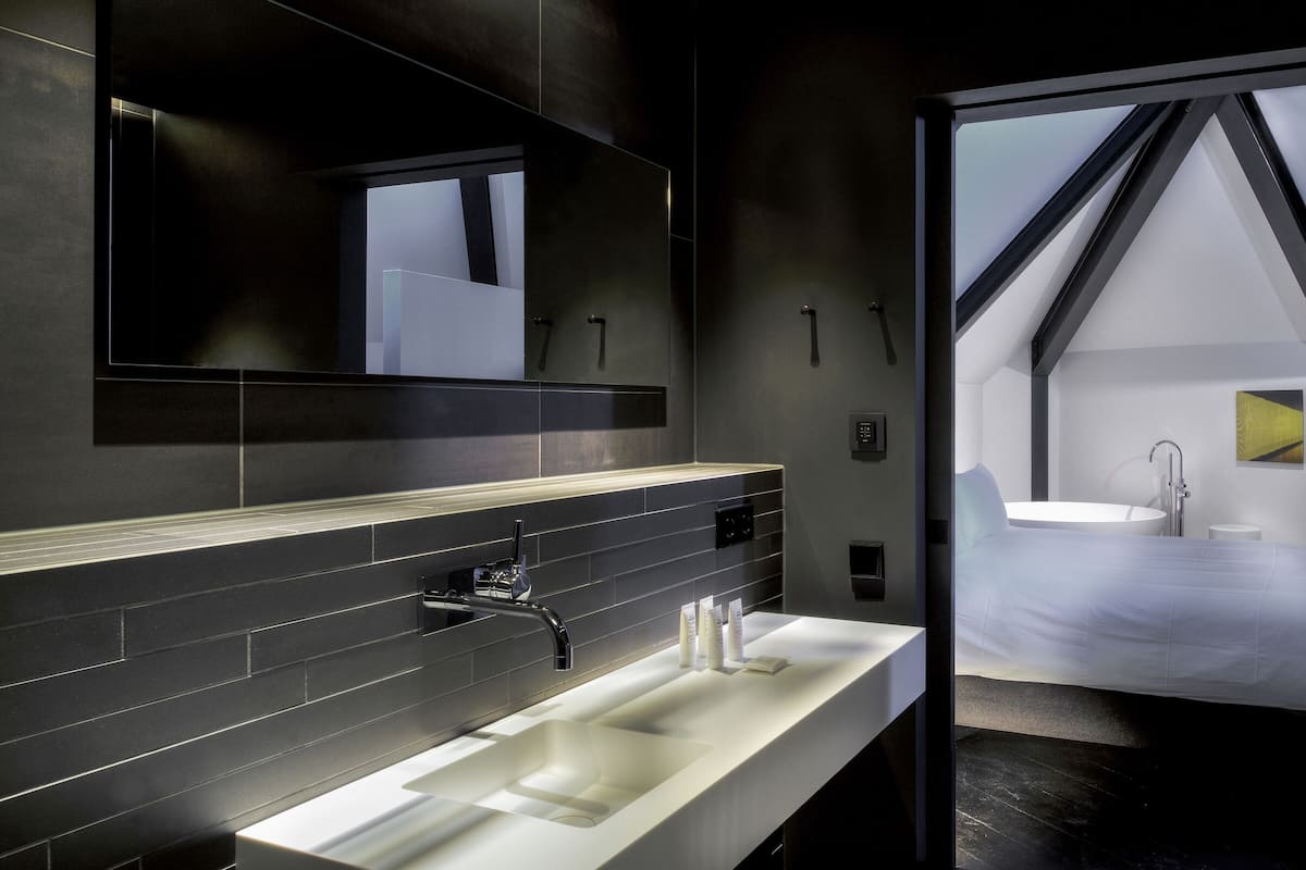 A modern bathroom with a large sink, a mirror, and a shower area visible through a doorway.