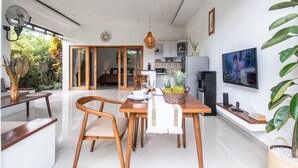 A modern kitchen with white cabinets, a dining area with wooden furniture, and a TV mounted on the wall.