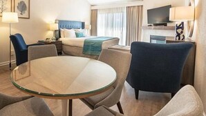 A hotel room with a bed, a TV, a desk, and a round glass table.