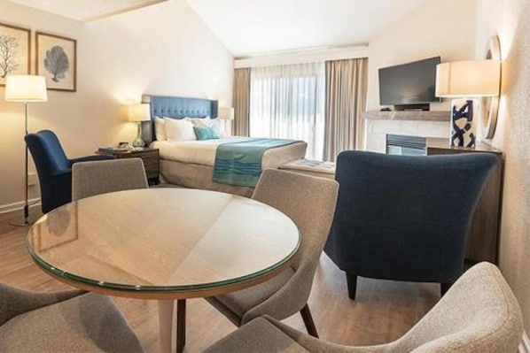A hotel room with a bed, a TV, a desk, and a round glass table.