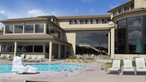 A modern building with a swimming pool, lounge chairs, and large windows.