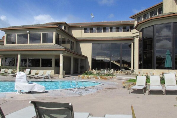 A modern building with a swimming pool, lounge chairs, and large windows.