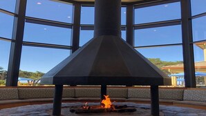 A stone fire pit with a chimney structure in a room with large windows.
