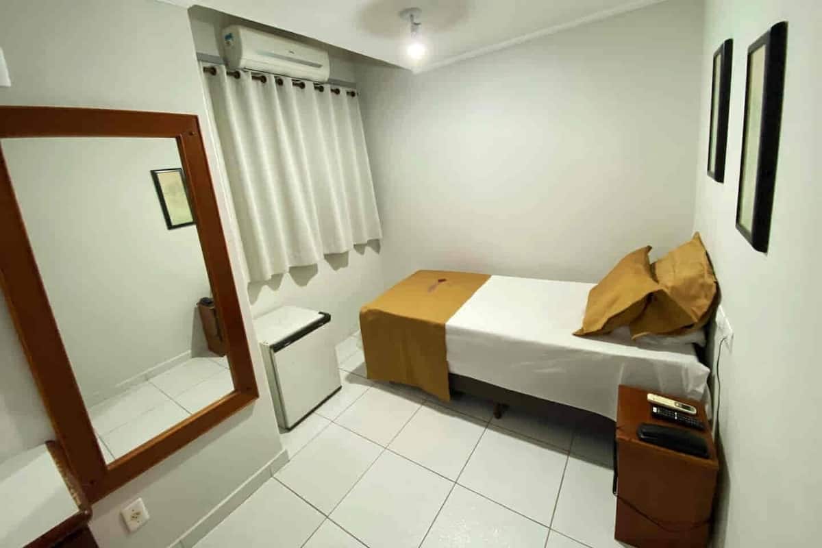 A small, clean room with a bed, a small table, a mirror, and a window with curtains.