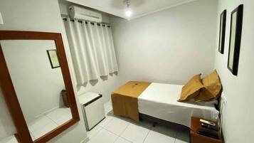 A small, clean room with a bed, a small table, a mirror, and a window with curtains.