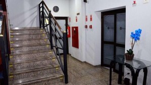 Una escalera con barandilla, un reloj y equipo de seguridad contra incendios en la pared.