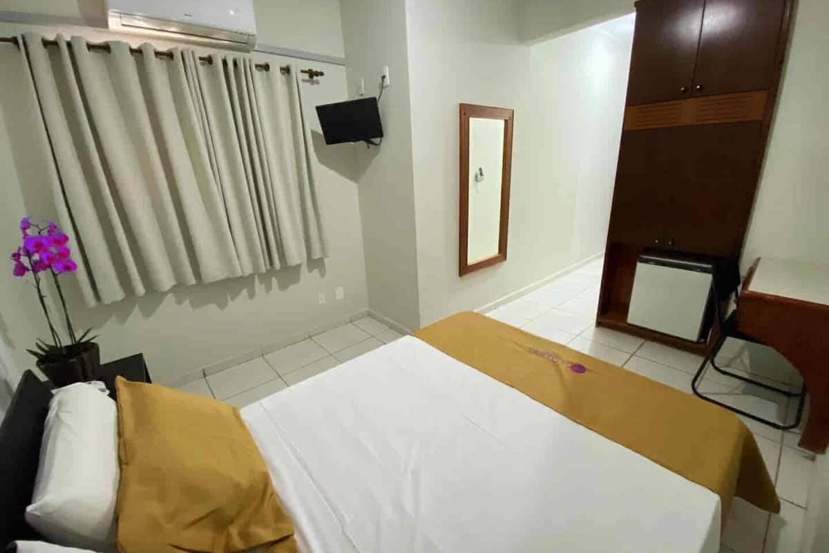 A hotel room with a bed, a desk, a chair, a TV, and a wardrobe.