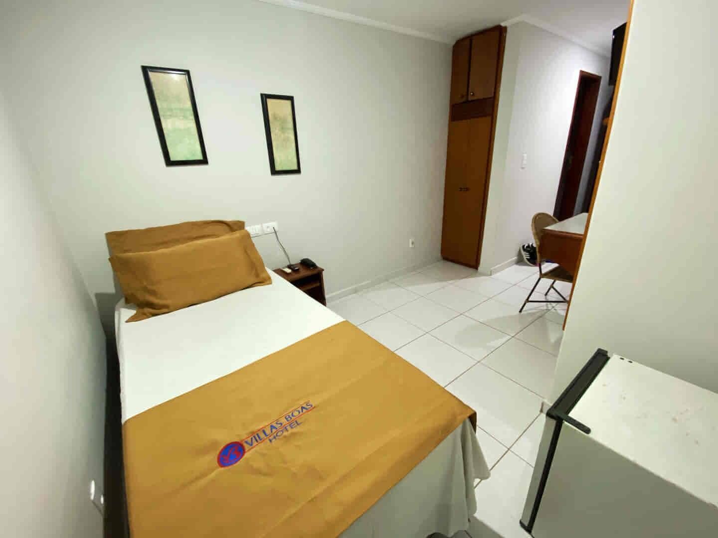 Habitación de hotel con una cama, un escritorio y una silla. Hay dos cuadros en la pared.