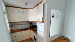 Cocina compacta con armarios blancos, lavadora, microondas y refrigerador pequeño.