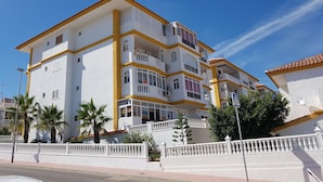 Un edificio de varios pisos con balcones, paredes blancas y detalles en amarillo.