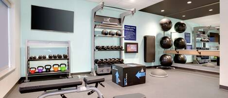 A fitness center with exercise equipment, dumbbells, kettlebells, and a mirrored wall.