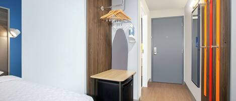 A compact hotel room with a bed, a small table, a wardrobe, and a mirror.