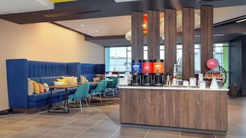 A modern hotel lobby with a blue sofa, teal chairs, a wooden reception desk, and a coffee station.