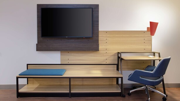 A modern office space with a flat-screen TV mounted on a wooden wall, a desk with a chair, and a red accent lamp. - Tru by Hilton Audubon Valley Forge (Audubon)