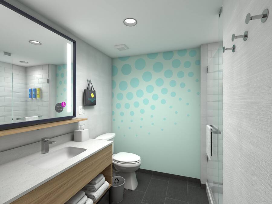 A modern bathroom with a white sink, mirror, and toilet. There is a towel rack with folded towels and a trash can.