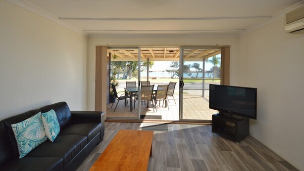 A living room with a sofa, a coffee table, and a TV. There is a sliding glass door leading to an outdoor patio with a table and chairs. - Kalbarri Waters A - Kalbarri, WA (Kalbarri)