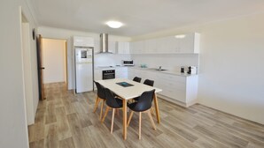 A modern kitchen with white cabinets, a dining table with four chairs, and a microwave. - Kalbarri Waters A - Kalbarri, WA (Kalbarri)