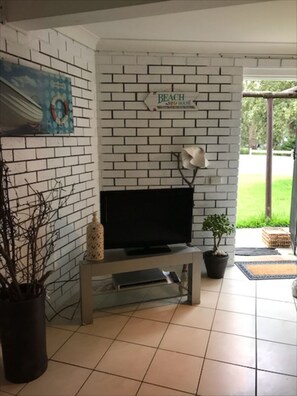 Relax in this stylish living room with a flat-screen TV, side table, and potted plant, offering a view of the surrounding green landscape.