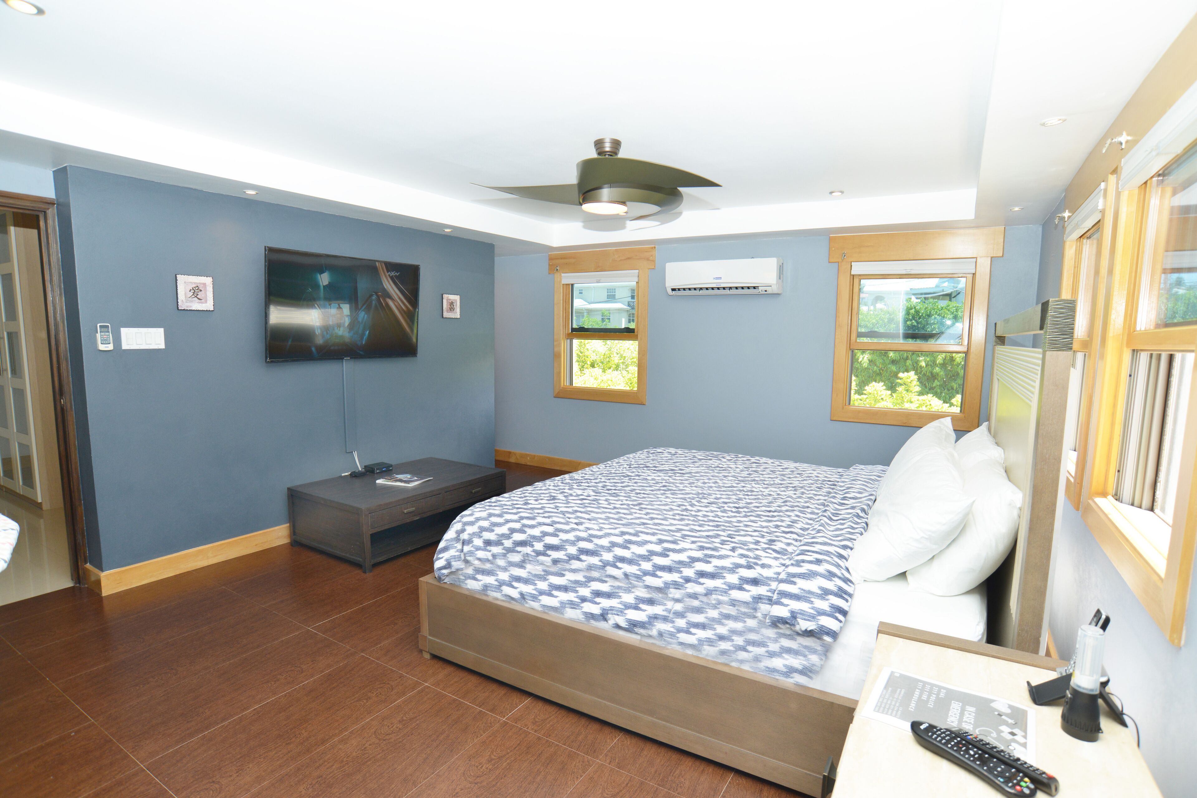 Une chambre à coucher avec un lit, une télévision, un ventilateur de plafond et une fenêtre.