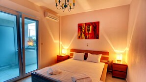 A hotel room with a large bed, two bedside tables, a ceiling light, a wall-mounted artwork, and a sliding glass door leading to an outdoor area. - StayInn Villa Bellevue (Nestos)
