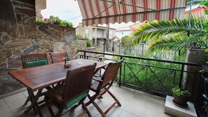 An outdoor patio with a wooden table and chairs, stone walls, and a view of a residential area with houses and greenery. - StayInn Villa Bellevue (Nestos)