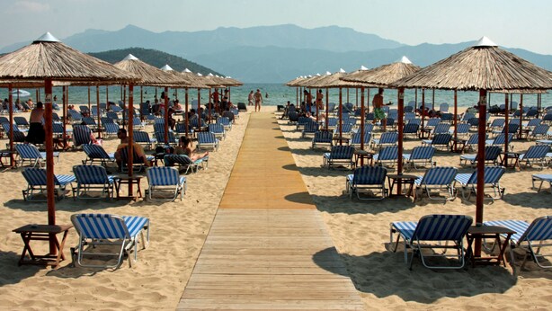 A beach with rows of blue and white striped lounge chairs and thatched umbrellas. - StayInn Villa Bellevue (Nestos)