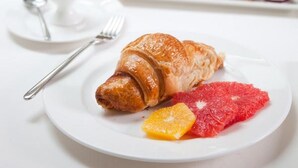 A breakfast setting with a croissant, grapefruit, and orange slices on a plate, a glass of orange juice, and a small vase with flowers. - StayInn Villa Bellevue (Nestos)