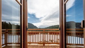 A wooden deck with glass doors leading to a view of a lake and mountains.