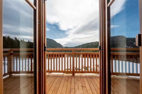 Eine Holzdielen-Terrasse mit Glastüren, die auf einen Blick auf einen See und Berge führt.