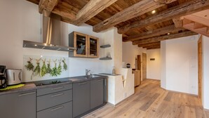 A modern kitchen with dark gray cabinets, a stainless steel range hood, and wooden beams on the ceiling.