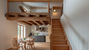 A dining area with wooden chairs and a table, a staircase, and a kitchen in the background.