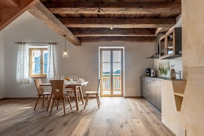 Ein Holzespeisetisch mit Stühlen, eine Küche mit Schränken und ein großes Fenster mit Ausblick.