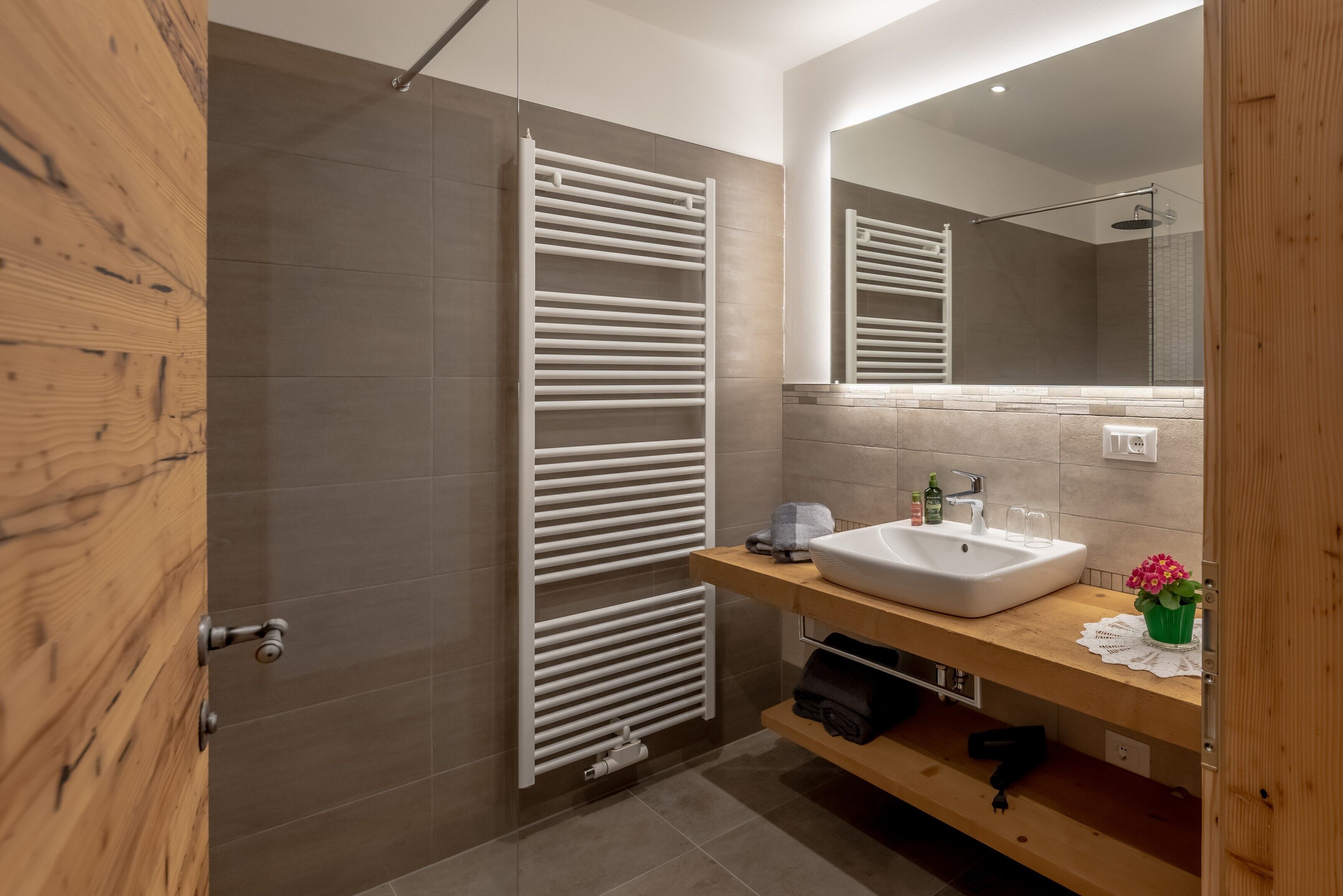 A modern bathroom with a wooden door, a white towel rack, a sink, and a mirror.