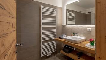 A modern bathroom with a wooden door, a white towel rack, a sink, and a mirror.