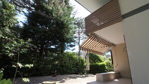 Een terras met een stenen vloer, een houten pergola en een grote boom.