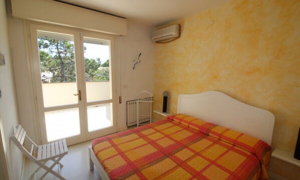 A bedroom with a bed, a chair, a window, and an air conditioning unit.